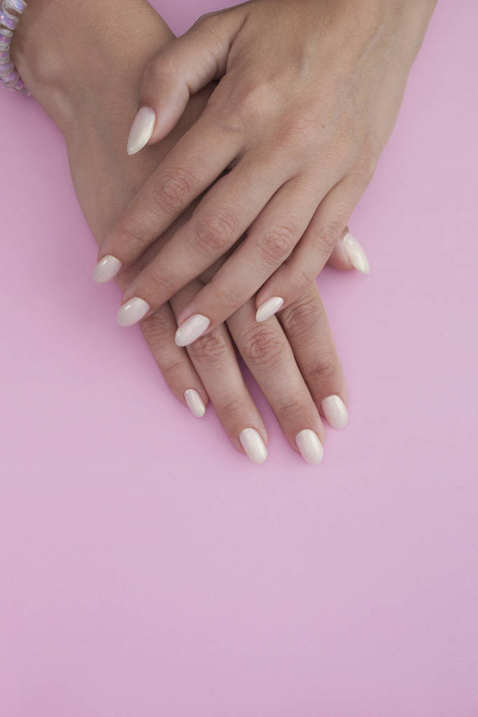 Gelooide handen van een jonge vrouw met een lichte manicure op een roze achtergrond. Nagellak - Foto, afbeelding