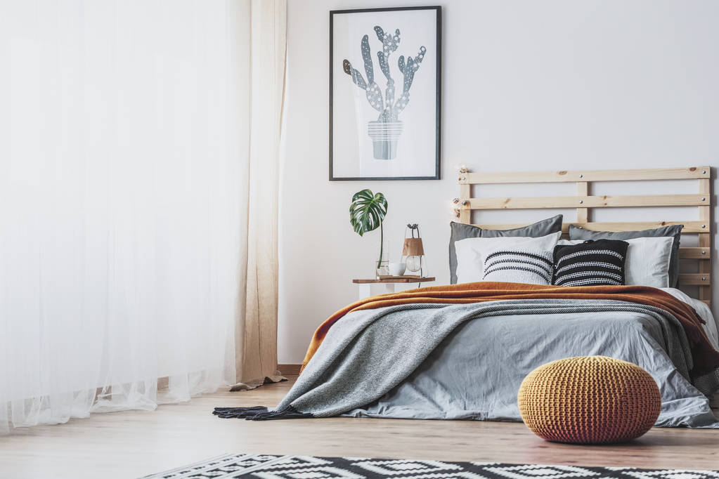 Pouf giallo davanti al letto in legno grigio all'interno della camera da letto con poster in cactus sopra foglia. Foto reale
 - Foto, immagini