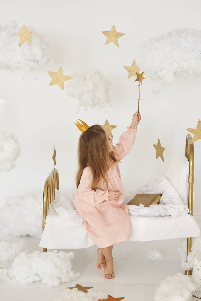 Piccola principessa con una bacchetta magica sul letto in una nuvola su uno sfondo bianco
 - Foto, immagini