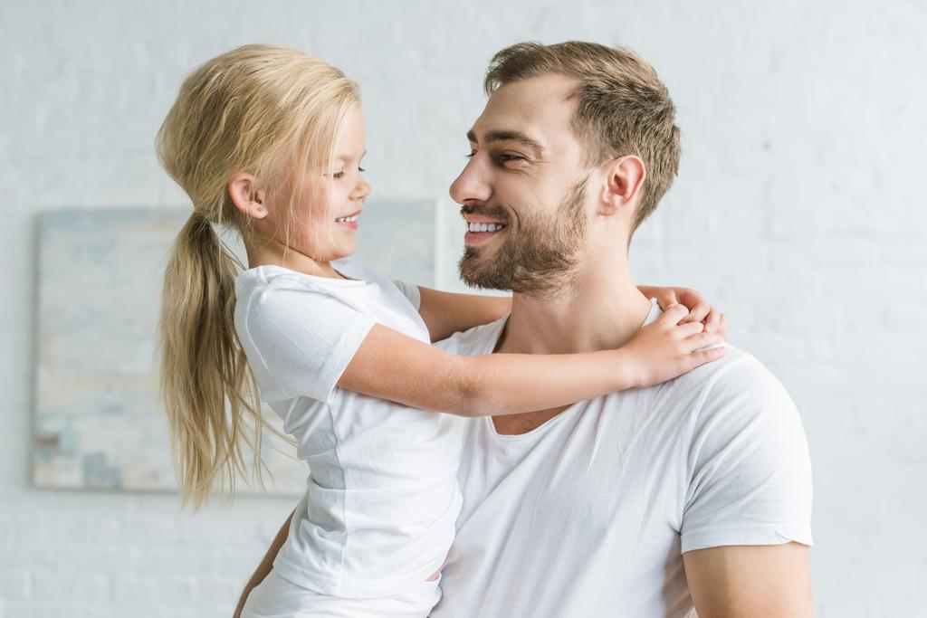 feliz padre y linda hijita abrazándose y sonriendo en casa
  - Foto, Imagen