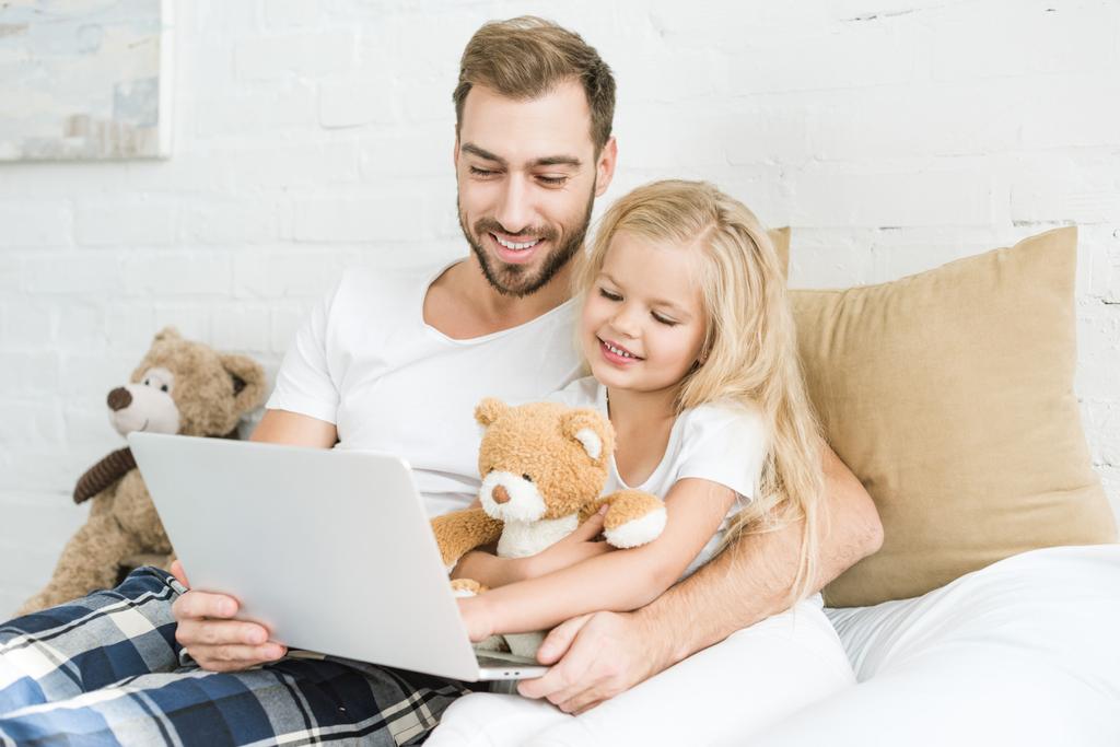happy father and cute little daughter using laptop together in bedroom  - Photo, Image