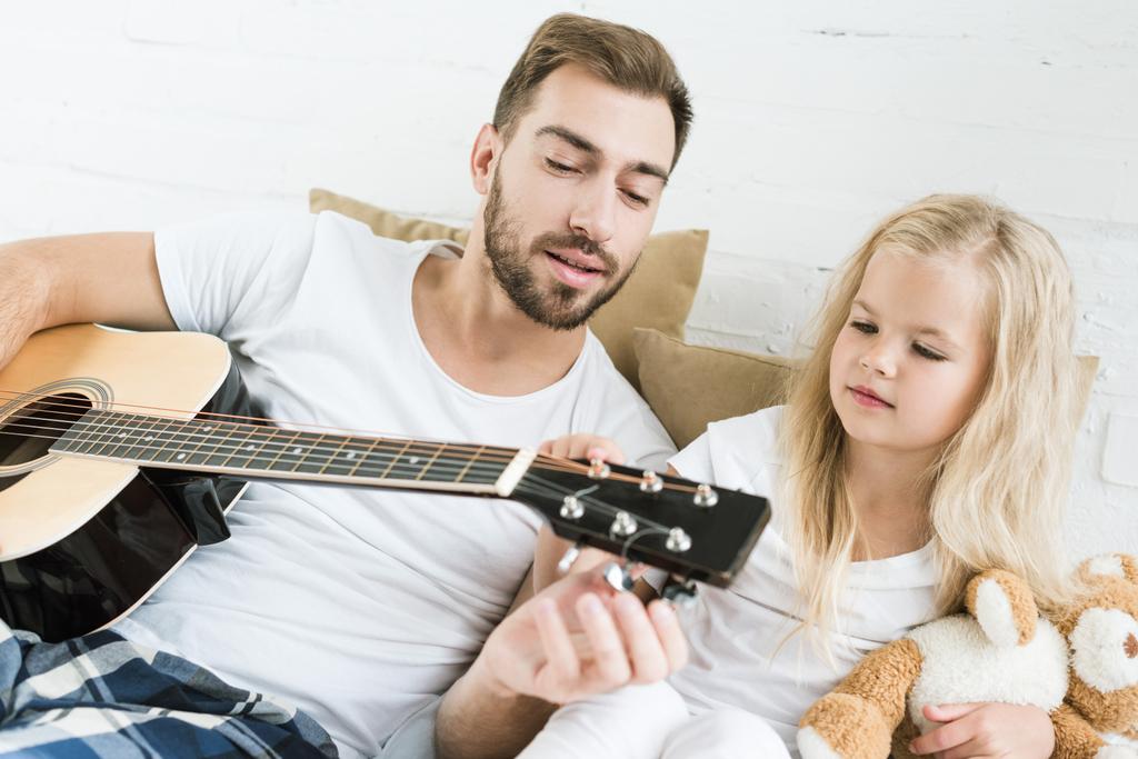 padre e carino piccola figlia suonare la chitarra acustica insieme sul letto
 - Foto, immagini