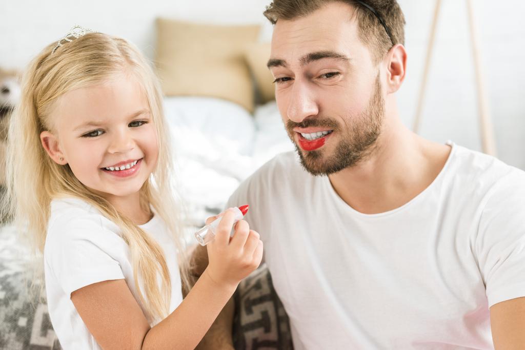 счастливый отец и милая маленькая дочь играют и наносят макияж дома
 - Фото, изображение