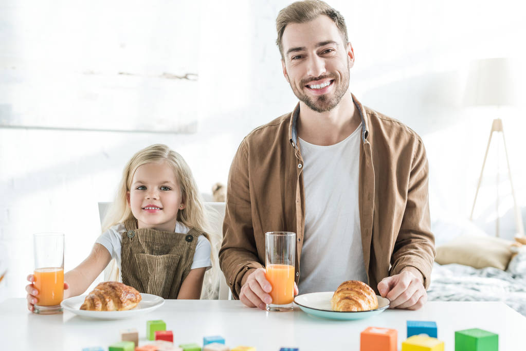 feliz padre y linda hijita sonriendo a la cámara mientras desayunan juntos
  - Foto, Imagen