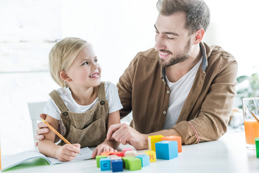 heureux père et fille souriant tout en apprenant avec des cubes en bois à la maison
 - Photo, image