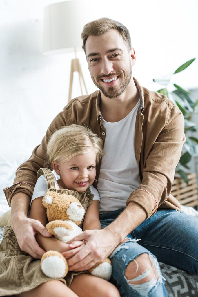 Glücklicher Vater und Tochter mit Teddybär sitzen zu Hause zusammen - Foto, Bild