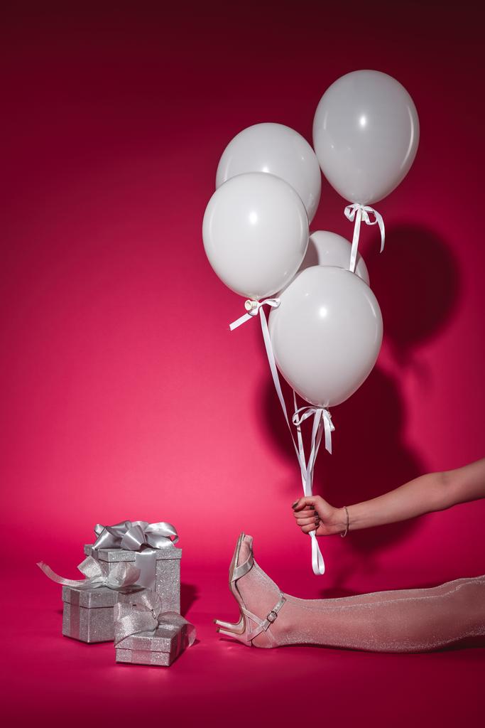 abgeschnittenes Bild eines Mädchens, das sitzt und ein Bündel weißer Luftballons mit Helium auf Burgund hält - Foto, Bild