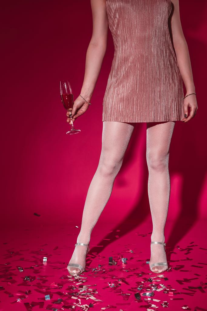 низкая секция женщины в платье, стоящей на конфетти с бокалом шампанского на вечеринке в Бургундии
 - Фото, изображение