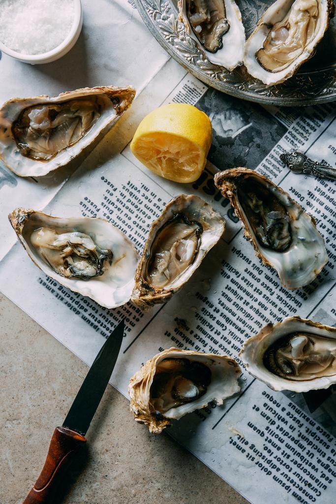 flat lay with oysters, lemon and knife on newspaper on grey surface - Photo, Image