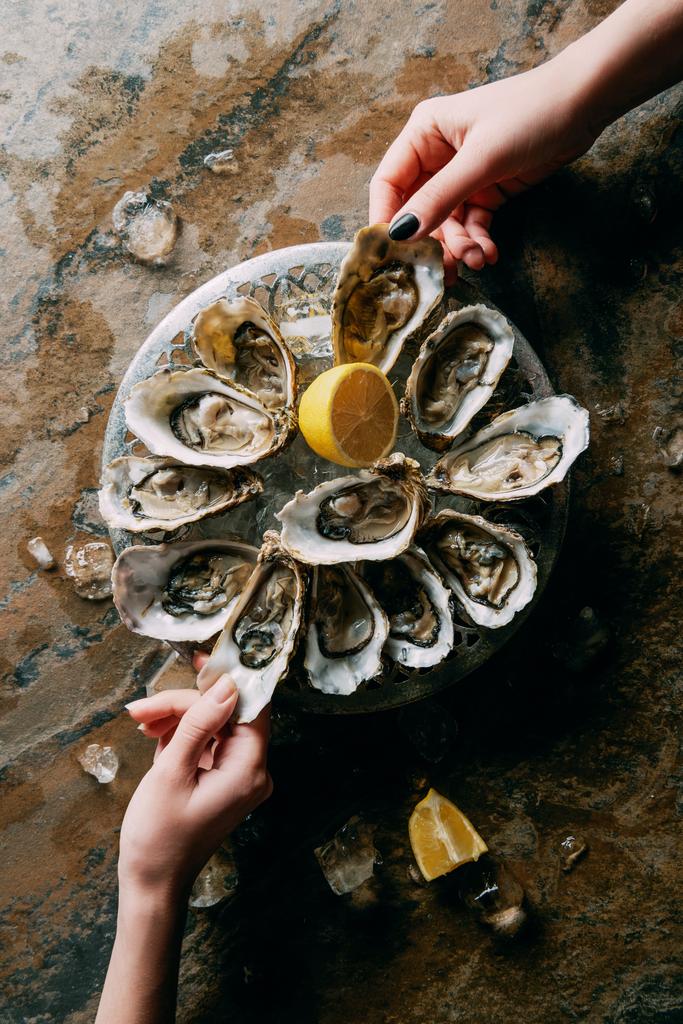 partial view of women at grungy tabletop with oysters, ice and lemon - Photo, Image