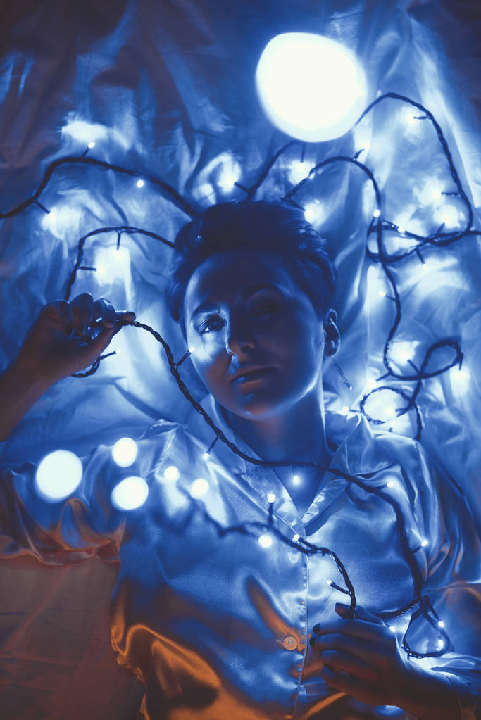 над головой вид женщины лежащей на кровати с рождественскими огнями вокруг
 - Фото, изображение