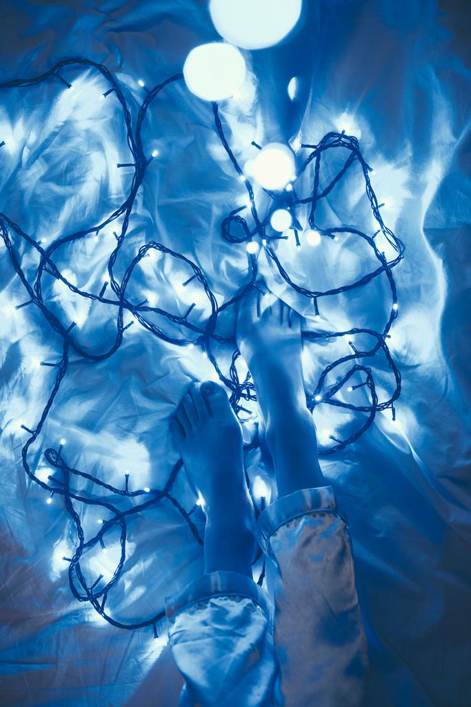 vágott lövés a nő pizsamában ágyon, ezen a környéken: kék karácsonyi fények - Fotó, kép