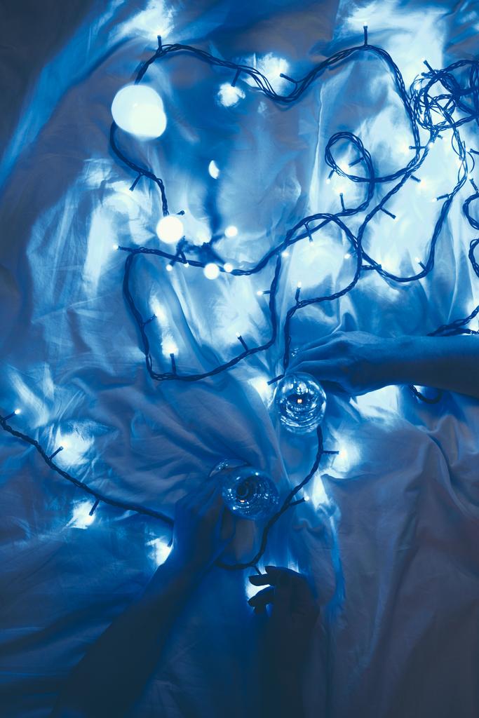 osittainen näkymä naisista, joilla on lasit samppanjaa sängyssä sinisillä juhlavaloilla
 - Valokuva, kuva