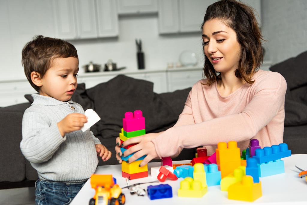 attractive happy woman and her little son playing with colorful plastic blocks at home - Photo, Image