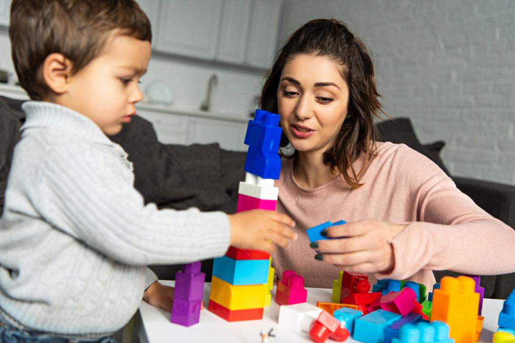 красивая женщина и ее маленький сын играют с красочными пластиковыми блоками дома
 - Фото, изображение