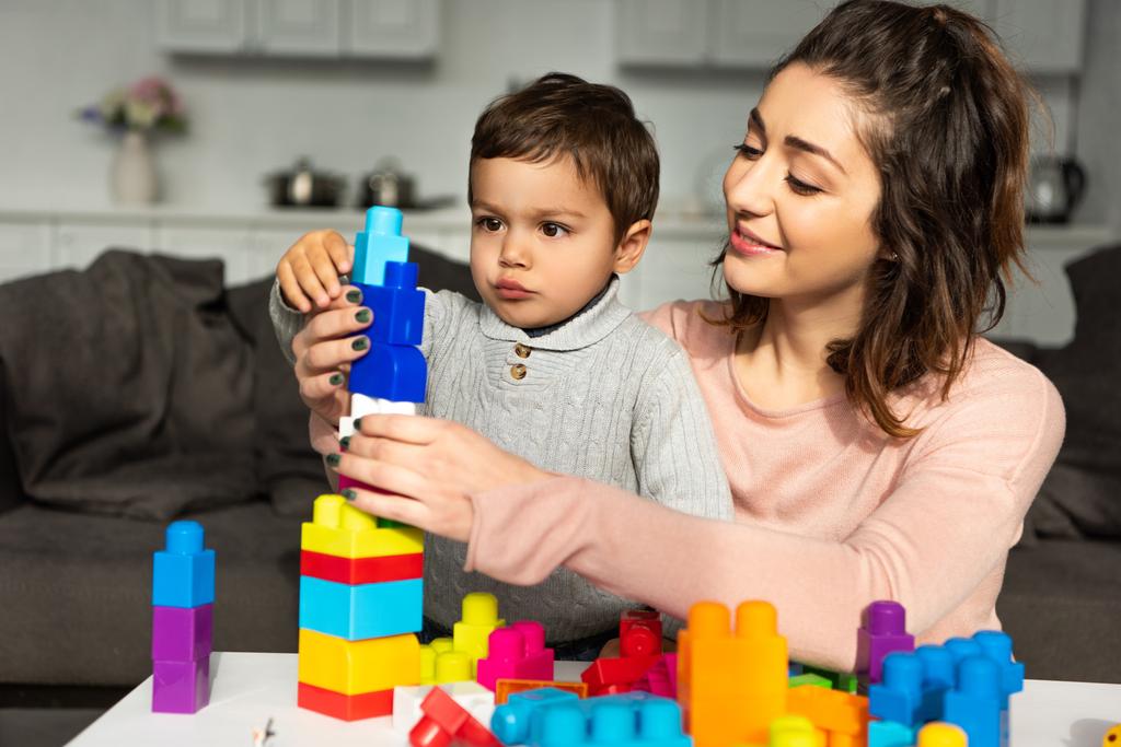 mãe sorridente e filho pequeno brincando com blocos de plástico coloridos em casa
 - Foto, Imagem