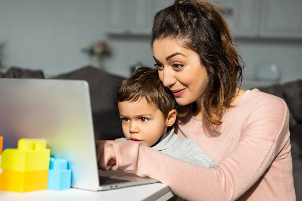 sürpriz küçük çocuk ve annesi evde oturma odasında masada dizüstü bilgisayar kullanarak - Fotoğraf, Görsel