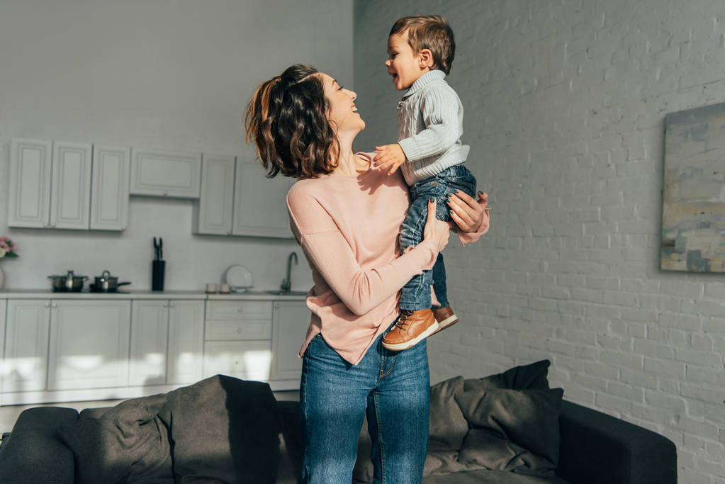 Улыбающаяся женщина держит очаровательного маленького сына на руках дома
 - Фото, изображение