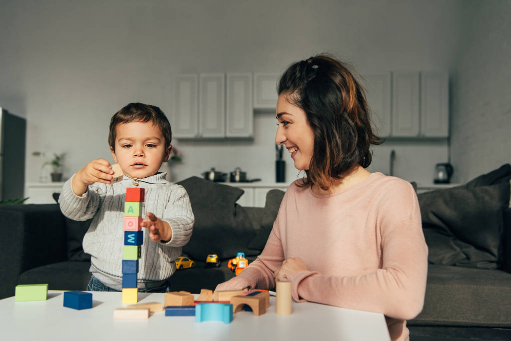 küçük çocuk ve annesi blok ahşap kule oyun evde oynarken seçici odak - Fotoğraf, Görsel