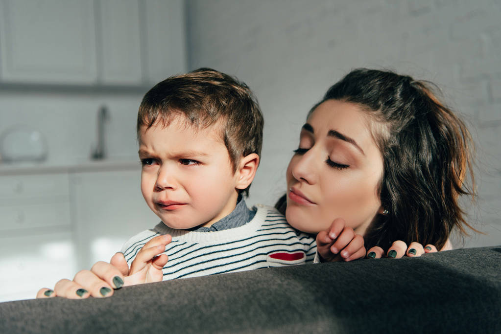close up view of mother cheering up crying little son on sofa at home - Photo, Image