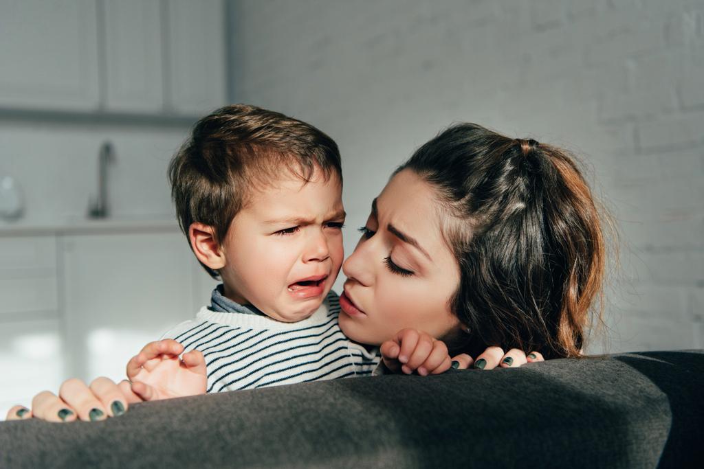 Selektiver Fokus der Mutter, die ihren weinenden kleinen Sohn auf dem heimischen Sofa aufmuntert - Foto, Bild