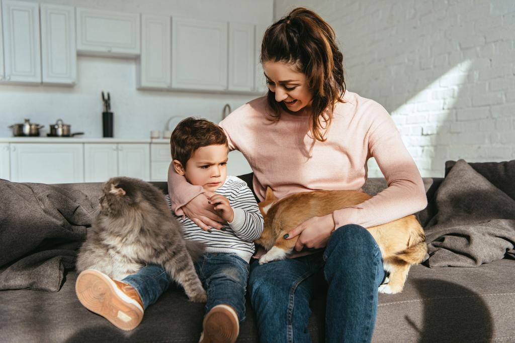 enfoque selectivo de la mujer y su hijo sentado en el sofá con gato y perro en la sala de estar en casa
 - Foto, Imagen