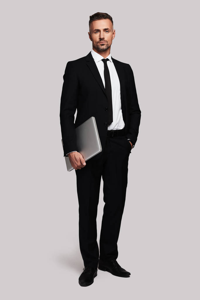 白い背景に立っているラップトップを保持しているビジネスの男性の完全な長さ - 写真・画像