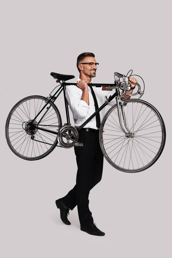 volledige lengte van de goed uitziende man die fiets op de schouder en wandelen op de grijze achtergrond - Foto, afbeelding