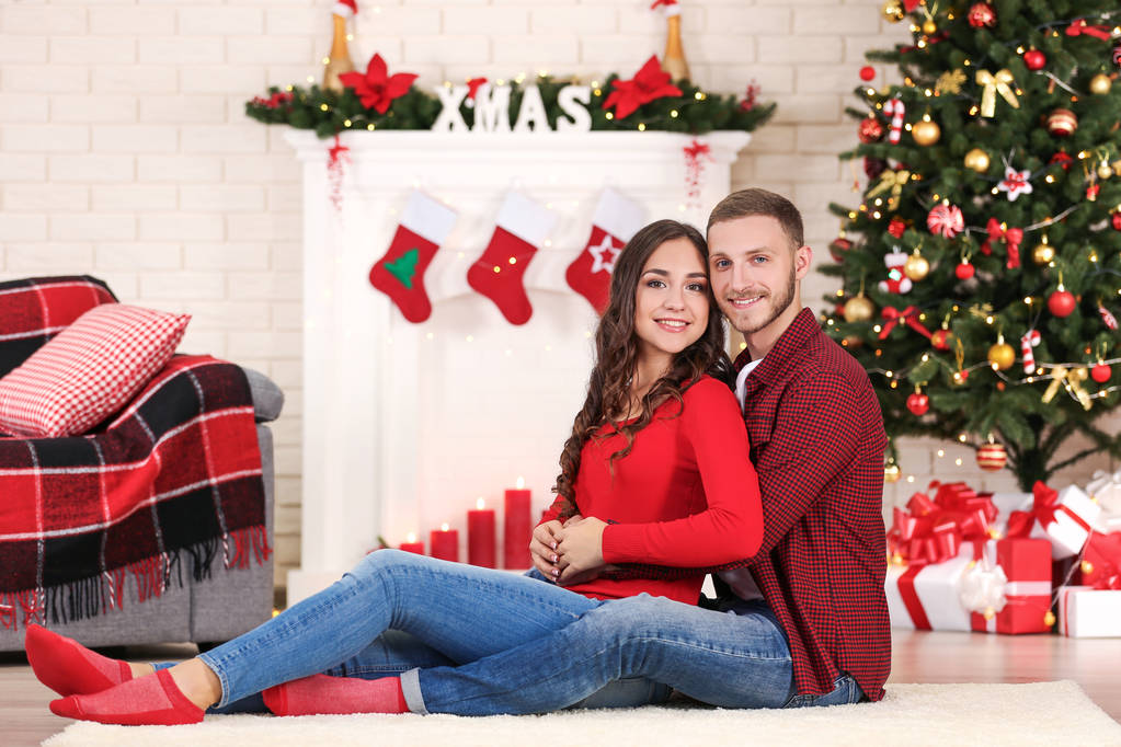 Feliz joven pareja sentada en casa cerca del árbol de Navidad
 - Foto, Imagen