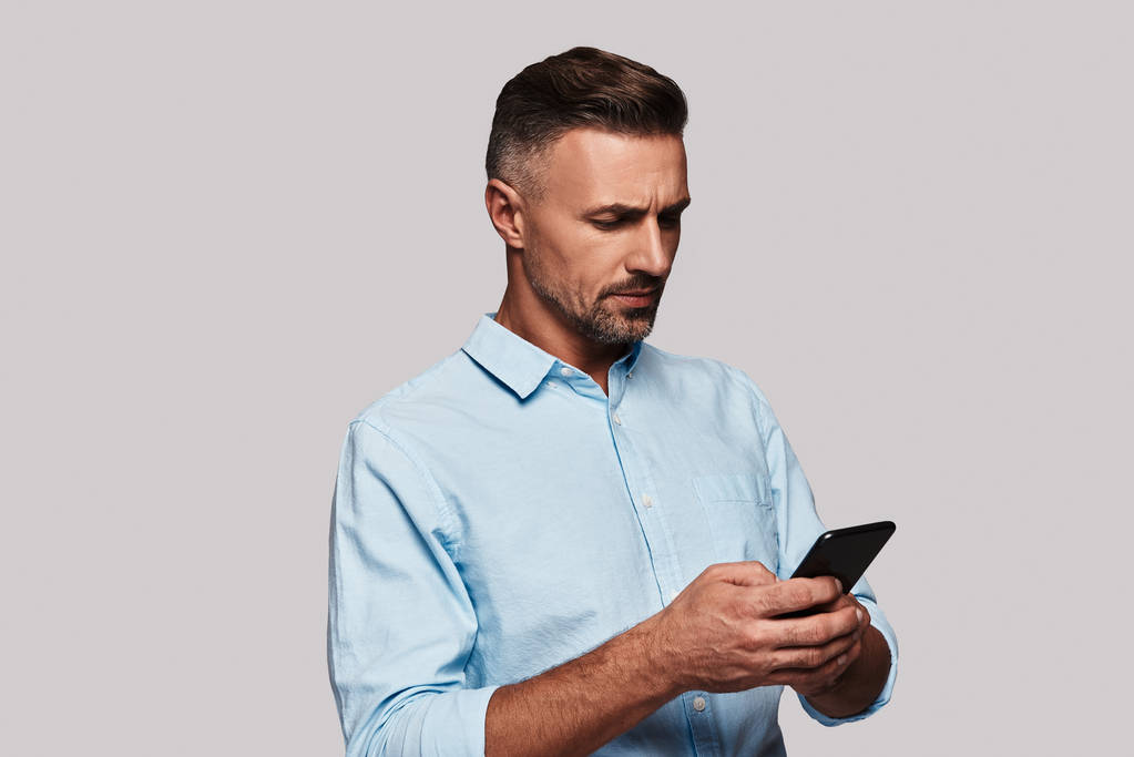 Hombre muy ocupado navegando por el teléfono inteligente y de pie sobre fondo gris
 - Foto, Imagen