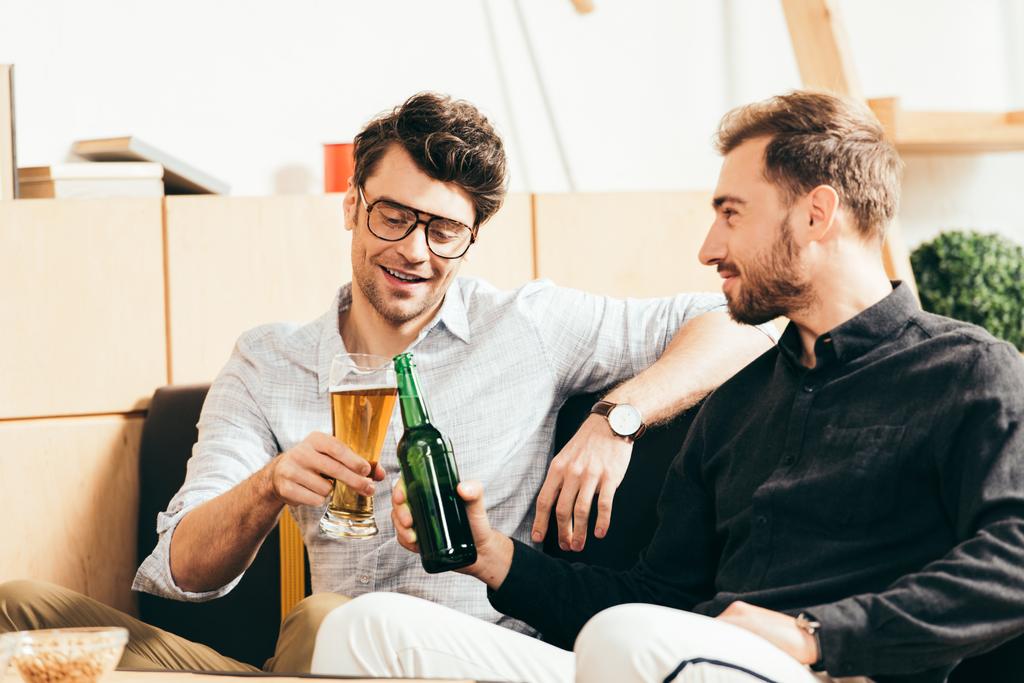 smiling friends clinking glass and bottle of beer in cafe - Photo, Image