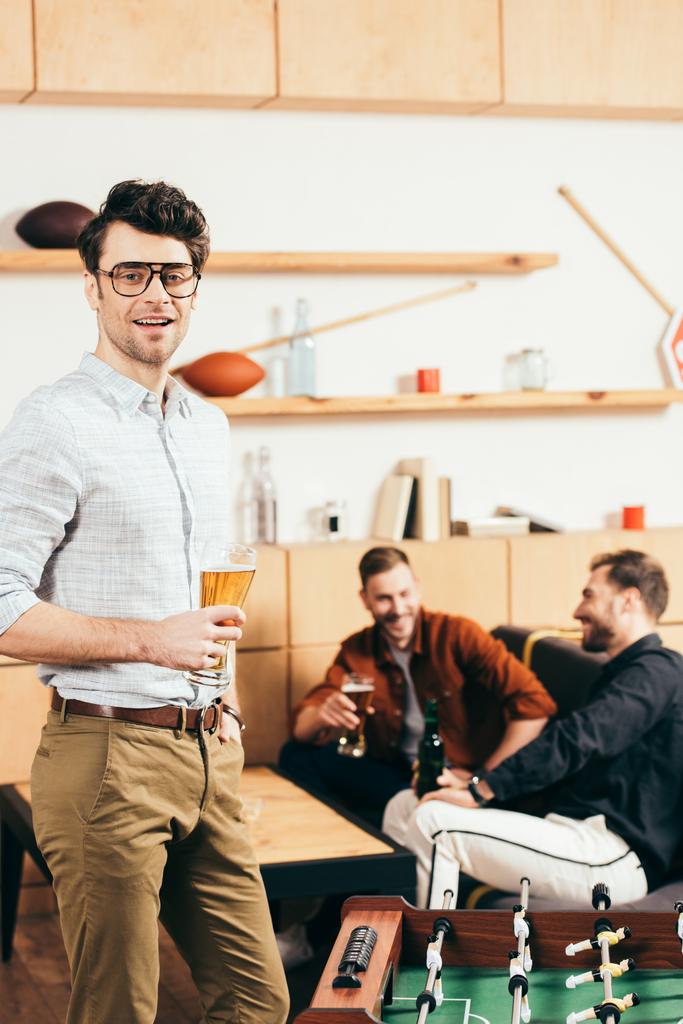 вибірковий фокус людини зі склянкою пива, дивлячись на камеру з друзями позаду в кафе
 - Фото, зображення