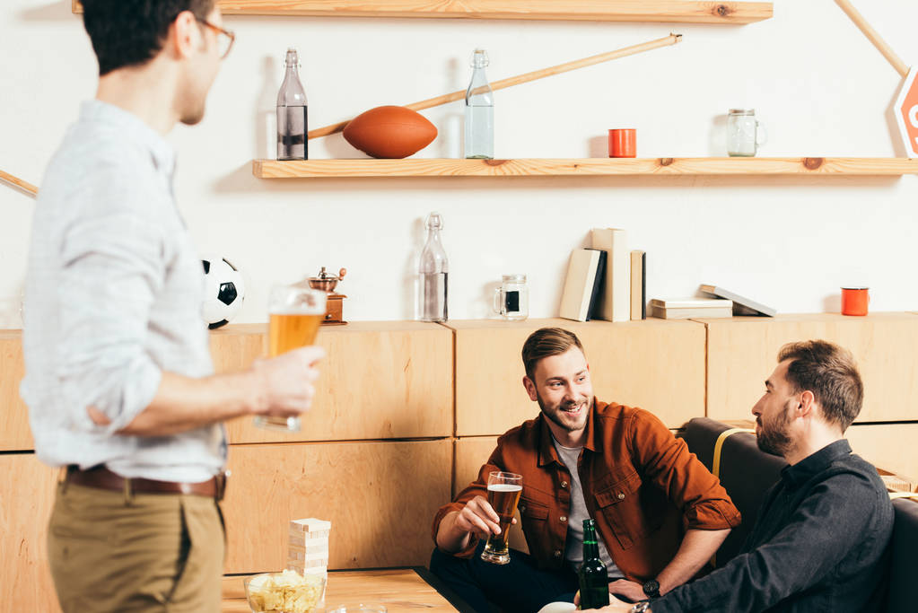 ο άνθρωπος με την μπύρα που βλέπουν το χαμόγελο φίλοι ακουμπά στον καναπέ στο καφέ - Φωτογραφία, εικόνα