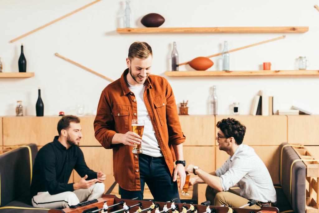 Selektive Fokussierung eines Mannes mit einem Glas Bier beim Blick auf Tablet-Fußball im Café mit Freunden im Hintergrund - Foto, Bild