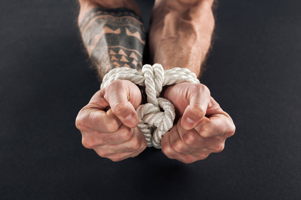 vista cortada de mãos masculinas amarradas com corda isolada em preto
 - Foto, Imagem