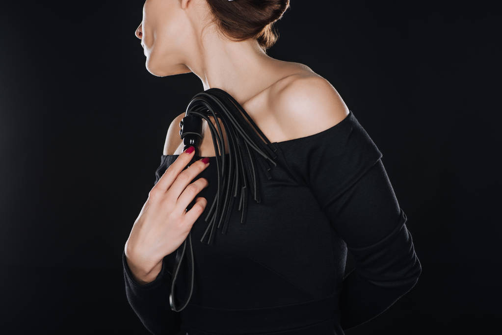 abgeschnittene Ansicht einer Frau mit lederner Peitsche, isoliert auf schwarz - Foto, Bild