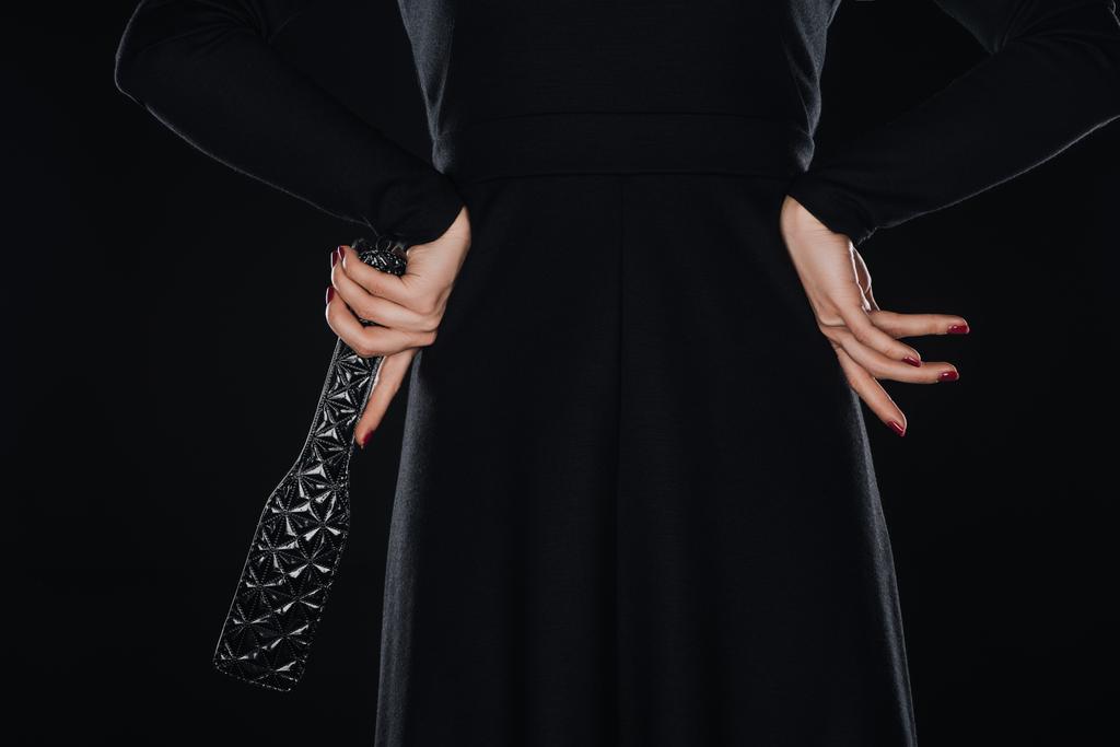 πίσω όψη της γυναίκας με τα χέρια στη μέση κρατώντας κουπί spanking απομονώνονται σε μαύρο - Φωτογραφία, εικόνα