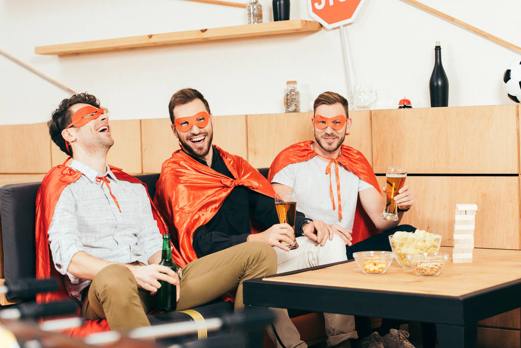 veselí přátelé v superhrdina kostýmy s pivem odpočívá společně v kavárně - Fotografie, Obrázek