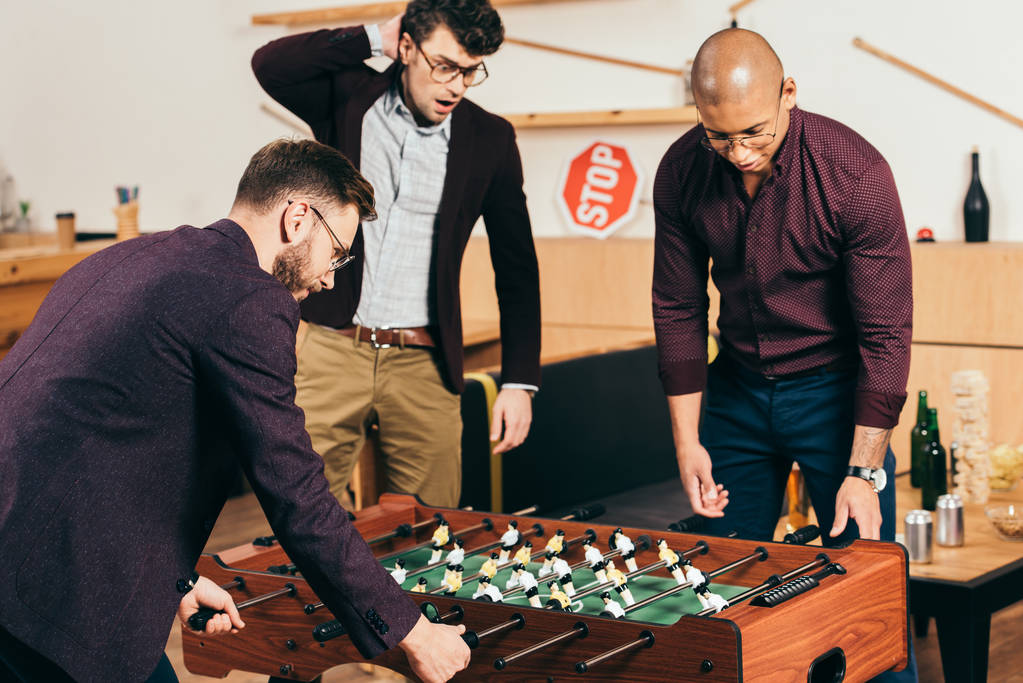 πολυφυλετικές επιχειρηματίες παίζοντας επιτραπέζιο ποδόσφαιρο ενώ ξεκουραζόταν σε καφετέρια - Φωτογραφία, εικόνα