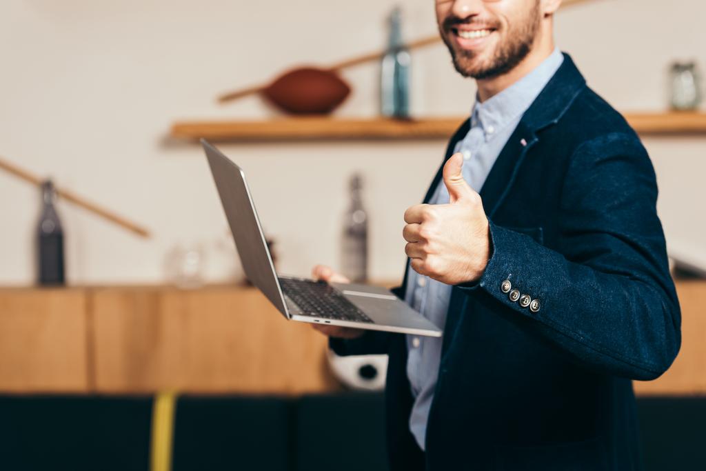 обрезанный снимок улыбающегося бизнесмена с ноутбуком, показывающим большой палец в кафе
 - Фото, изображение