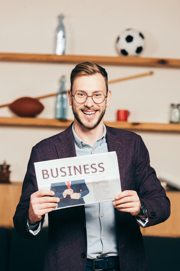 portrait of cheerful businessman showing newspaper in hands in cafe - Photo, Image