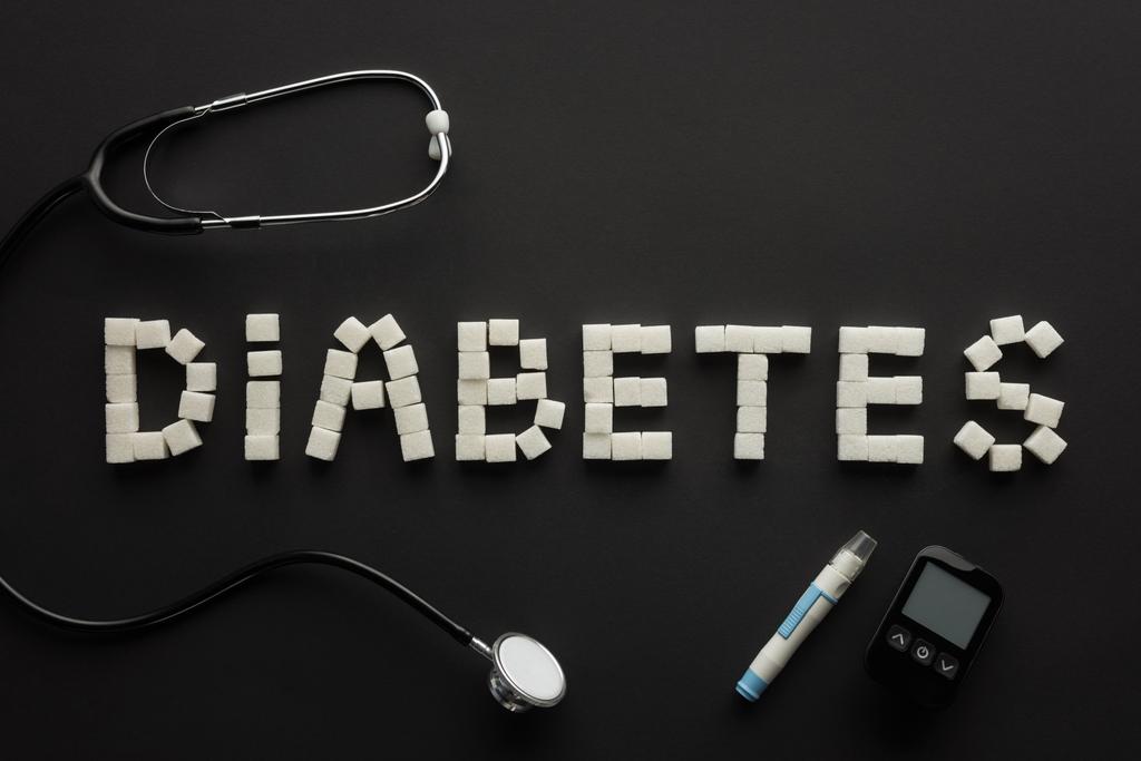 bovenaanzicht van "diabetes" letters gemaakt van suikerklontjes met medische apparatuur op zwart - Foto, afbeelding