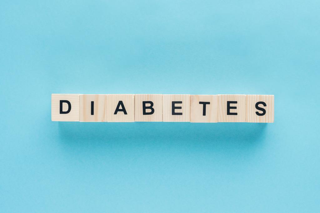 bovenaanzicht van "diabetes" letters gemaakt van houten kubussen in lijn op blauwe achtergrond - Foto, afbeelding