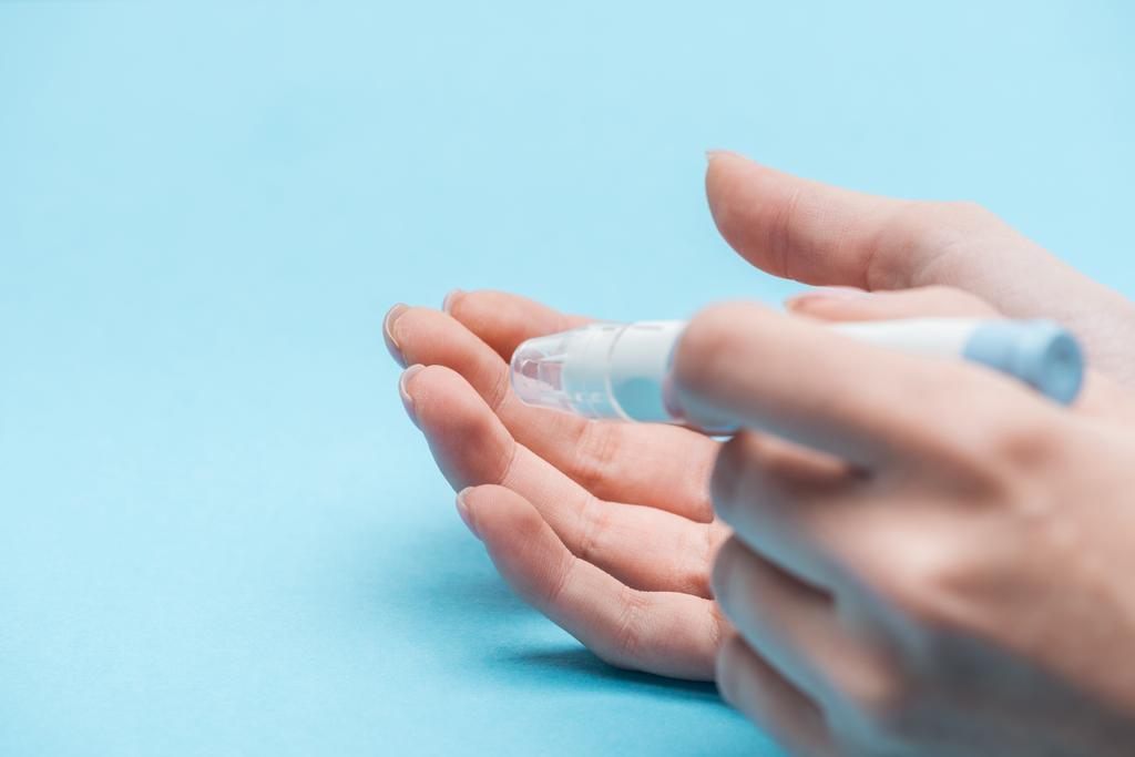 обрізаний вид жіночих рук, що тестують рівень глюкози з голкою на синьому фоні
 - Фото, зображення