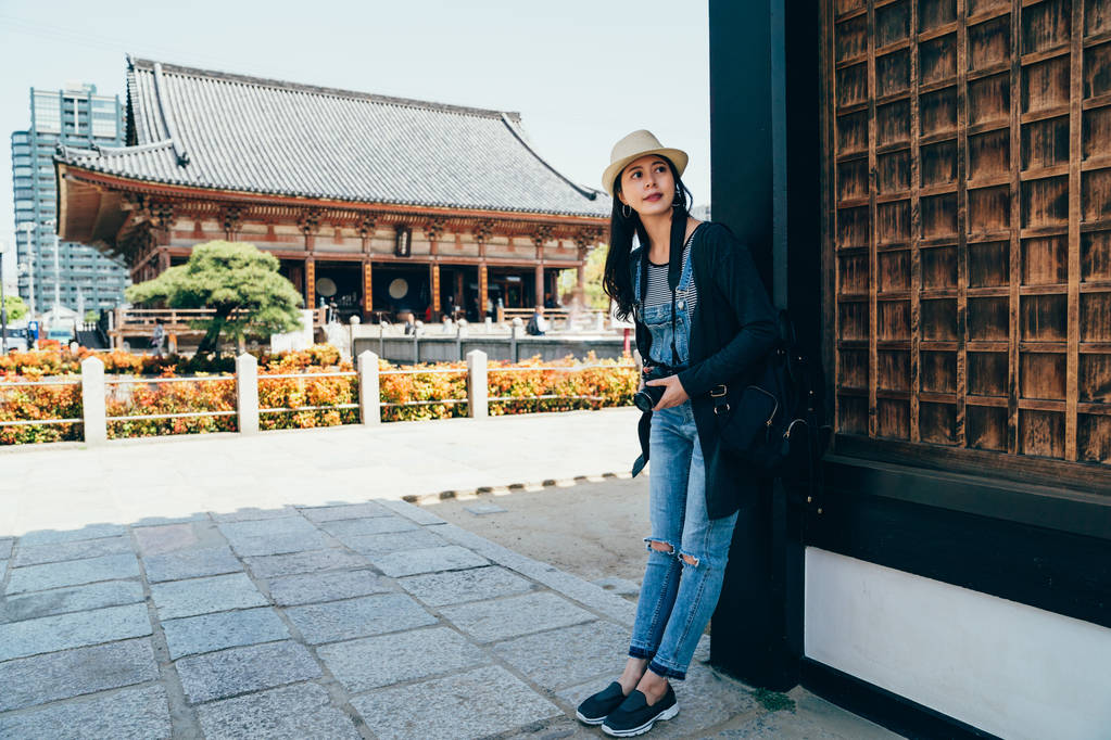 Turista asiático visitar o shitennoji no dia ensolarado contar com a parede sob a sombra do edifício do templo japonês de madeira. jovem fotógrafo relaxante em atrações osaka. Mulher alegre viagem japão
 - Foto, Imagem