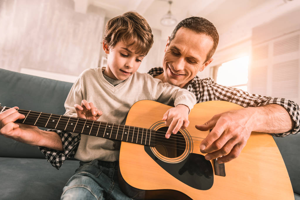 Staat volwassen musicus kritiseren van zijn zonen manier om gitaar te spelen. - Foto, afbeelding