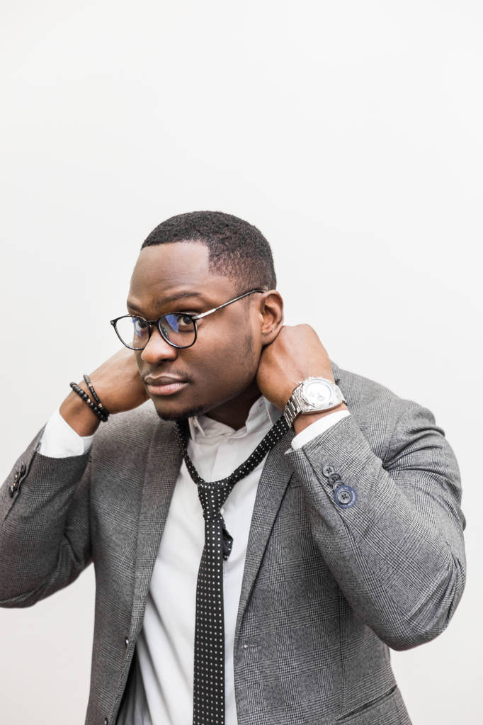 Молодой афроамериканский бизнесмен в сером костюме, завязывающий галстук на белом фоне
. - Фото, изображение