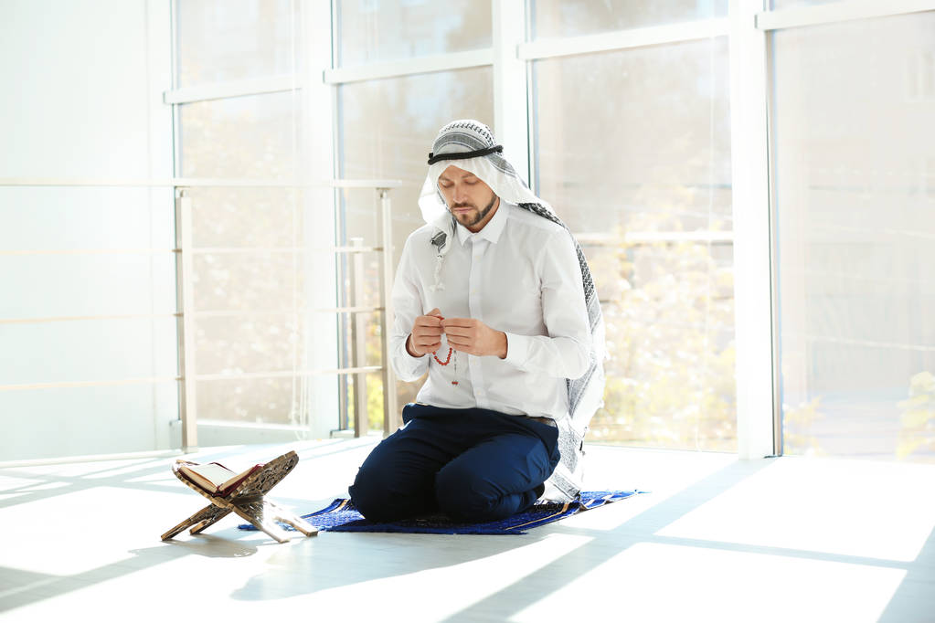 Hombre musulmán con el Corán rezando en la alfombra interior
 - Foto, imagen