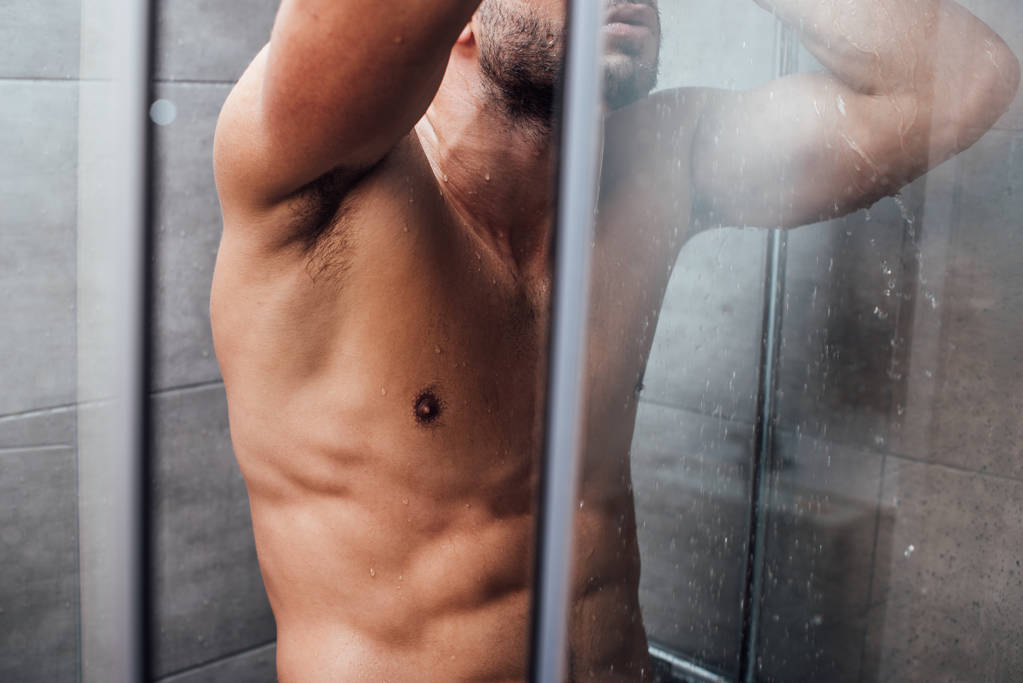 vista ritagliata dell'uomo muscolare che si fa la doccia in bagno
 - Foto, immagini