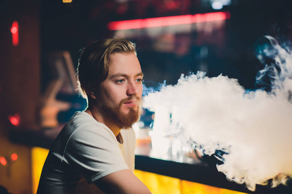 Молодой человек, курящий шишу в арабском ресторане - человек, вдыхающий дым от кальяна
. - Фото, изображение